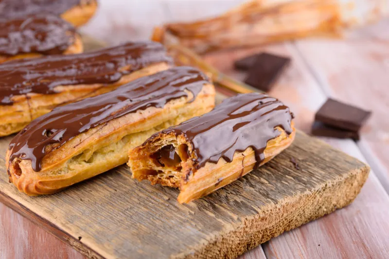 tasty and beautiful eclairs with chocolate on a wooden board appetizing dessert party supplies flat lay
