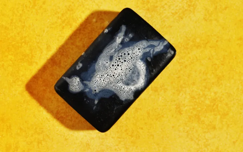 wet bar of black soap with bubbles on yellow bright background