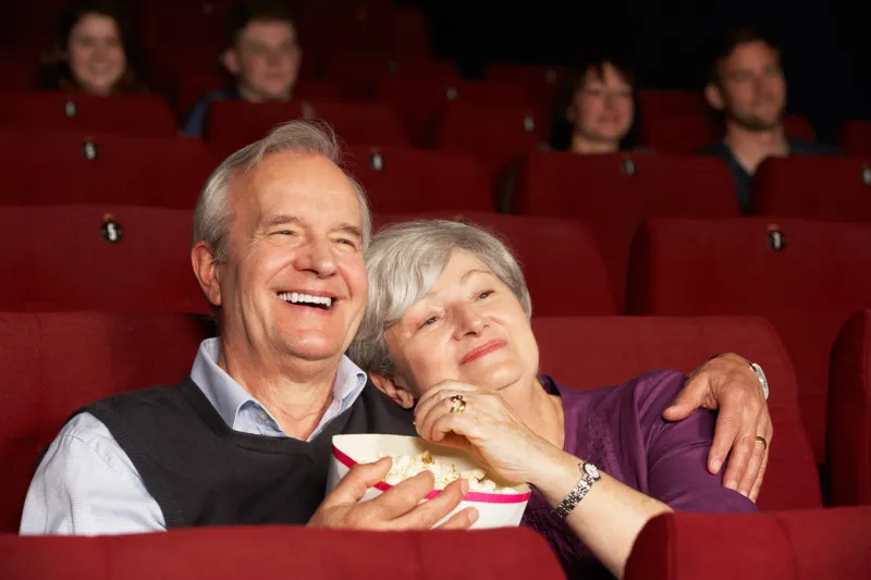 senior couple watching film in cinema laughing and eating popcorn