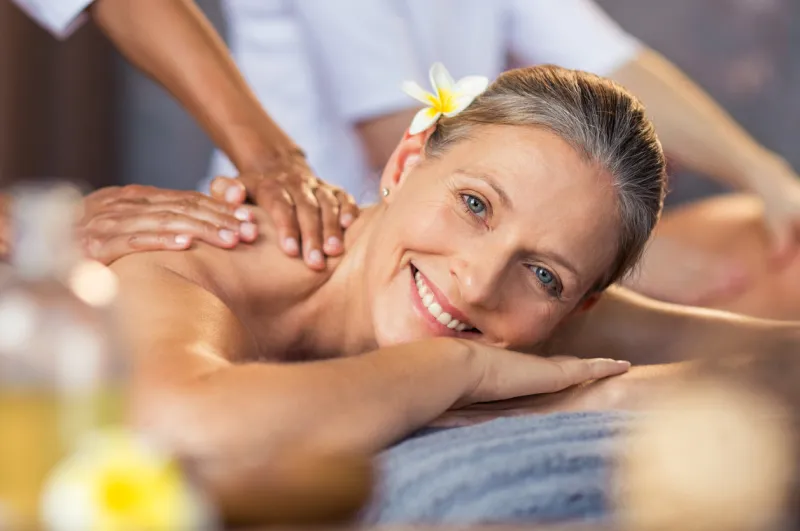 happy senior woman getting oil massage on her back at spa center portrait of senior woman receiving back massage closeup face of smiling mature woman relaxing on massage table and looking at camera