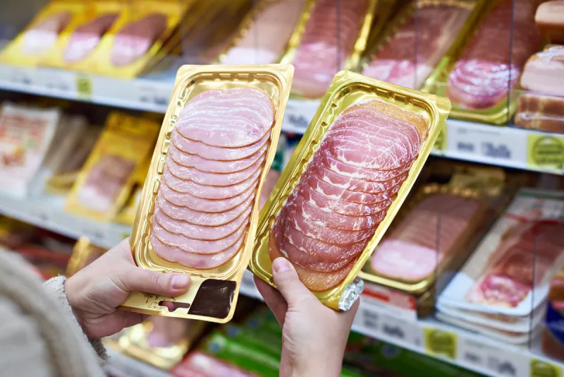 woman chooses a slice of ham and meat in vacuum package at the grocery store