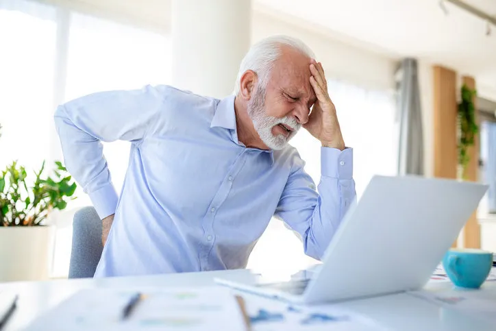 senior businessman working sitting at desk suffers from lower back pain damage of intervertebral discs, spinal joints, compression of nerve roots caused by wrong posture and sedentary work