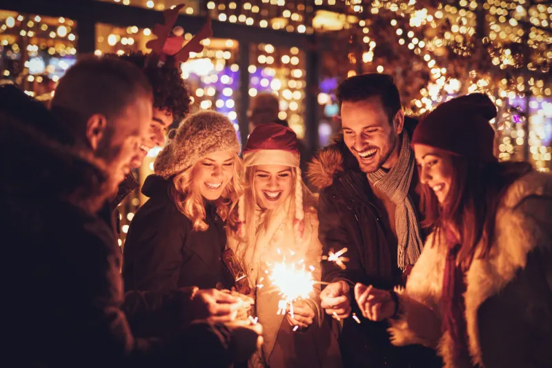 three couple with sparklers enjoying christmas outdoor party in the city street at night and with a lot of lights on background