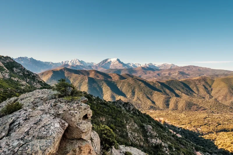 a rocky outcrop in the mountains of corsica at lama with the cinto massif and snow capped monte padru in the distance