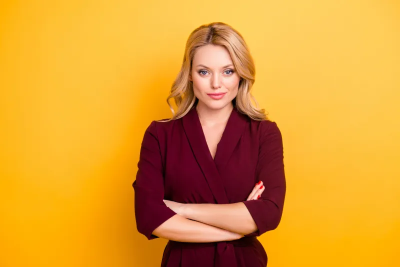 portrait of pretty charming woman in burgundy suit having her arms crossed looking at camera isolated on yellow background