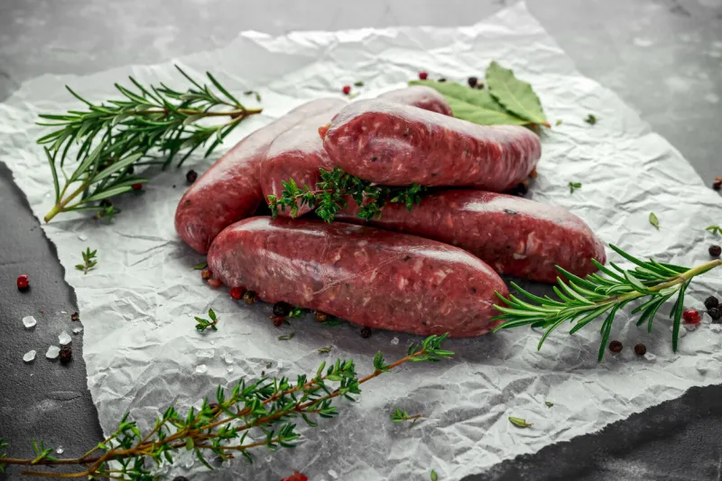 freshly made raw breed butchers sausages in skins with herbs on crumpled paper