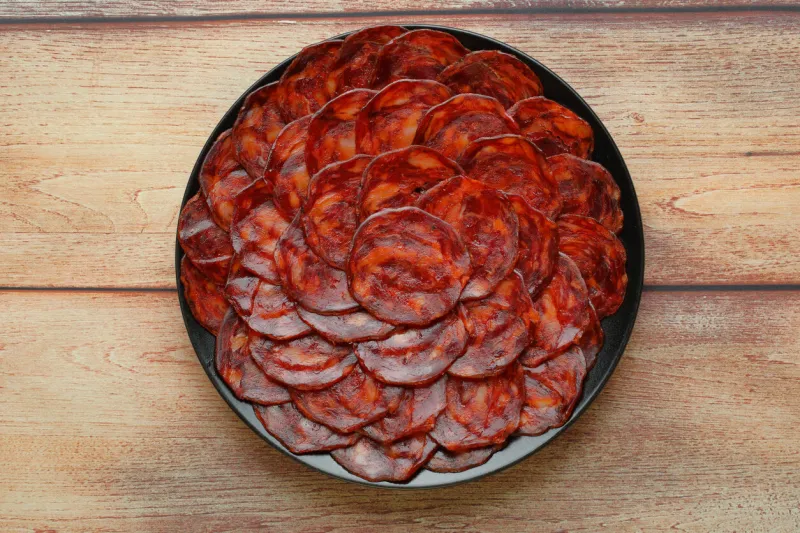 serving of acorn-fed iberian chorizo on black plate on rustic wooden table top view