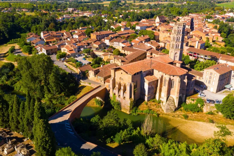 scenic aerial view of french commune of rieux-volvestre on bank of arize river at sunny summer day