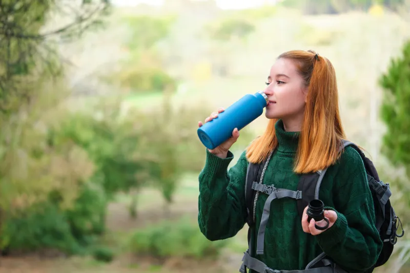 smiley hiker redhead young woman drinking water from bottle in the mountain wearing a backpack trekking concept