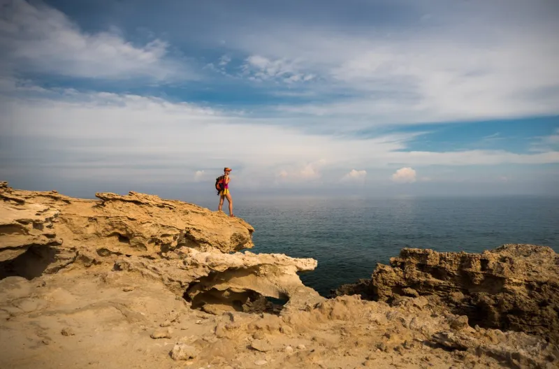 young woman hiker standing on top of the rocks and enjoying view of a blue lagoon near polis city, akamas peninsula national park, cyprus