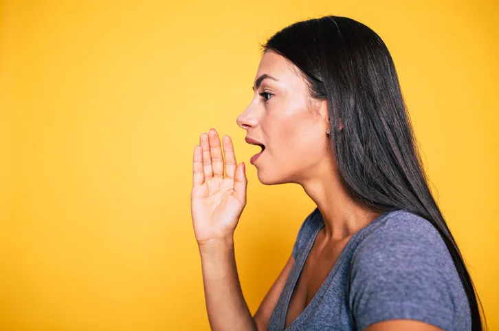 side view portrait of cute attractive young girl, woman is shouting something away or talks for someone isolated on yellow background