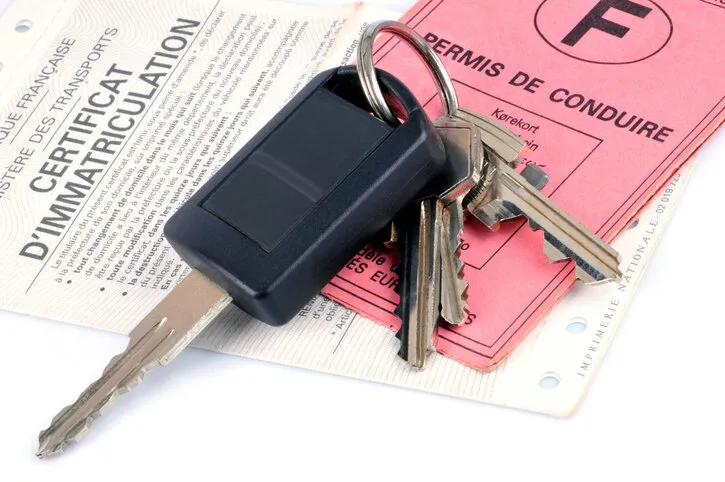 car key placed on a driver's license and a registration certificate on a white background