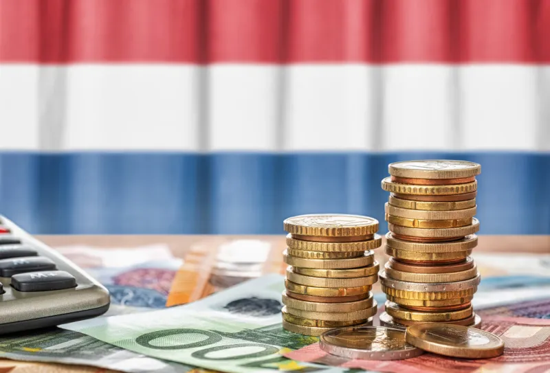 euro banknotes and coins in front of the national flag of the netherlands