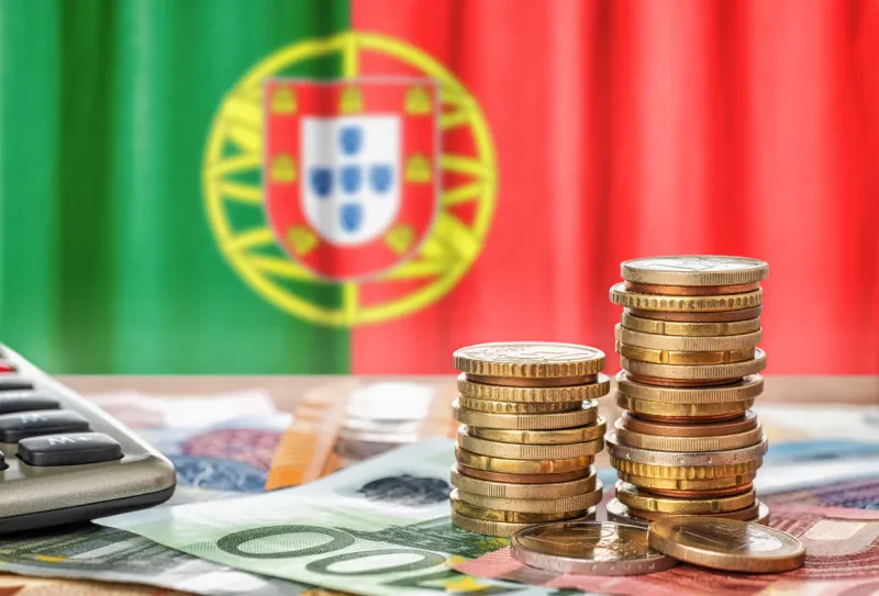 euro banknotes and coins in front of the national flag of portugal