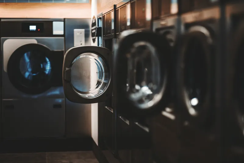 a dark laundry room with multiple wall embedded washing machines and dryers of different models and capacity, some washers doors are opened, selective focus, shallow depth of field, strong bokeh