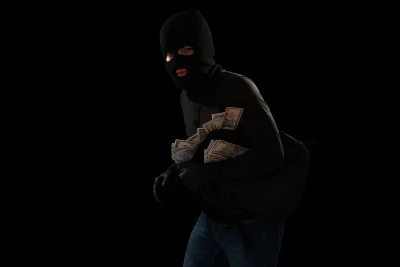 thief with a black mask breaking into a house and escaping after stealing a lot of money in a backpack