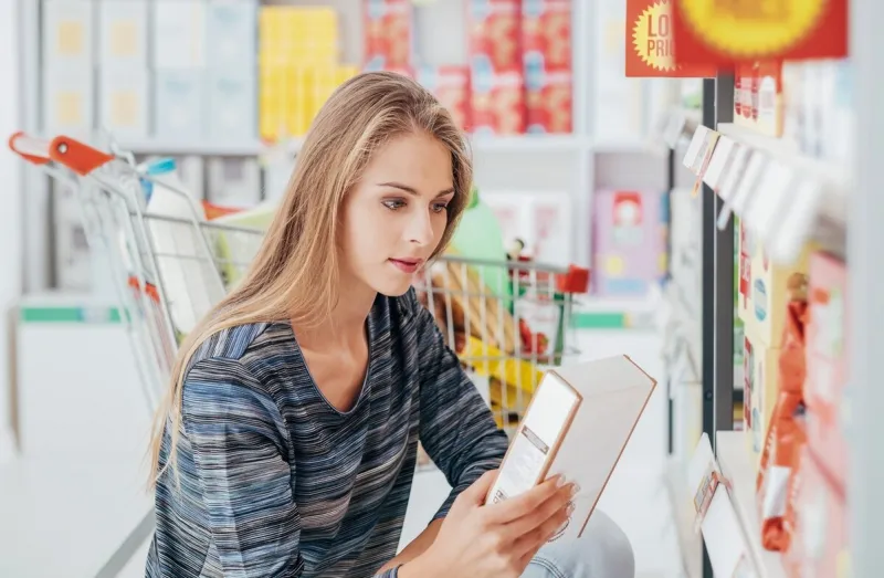 young woman doing grocery shopping at the supermarket and reading a food label with ingredients on a box, shopping and nutrition concept