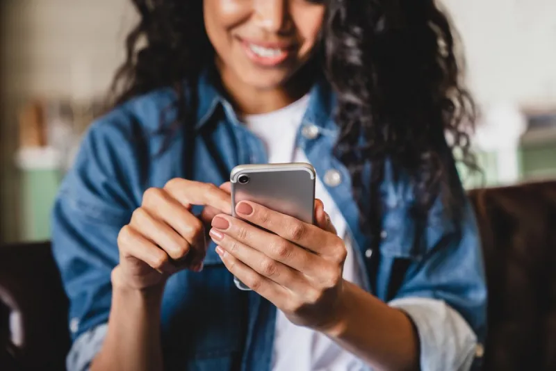 cropped shot of an african-american young woman using smart phone at home smiling african american woman using smartphone at home, messaging or browsing social networks while relaxing on couch