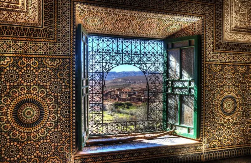 une fenêtre ornée dans la kasbah telouet au maroc donne sur les champs et les montagnes de l'atlas