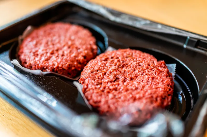 closeup of two raw uncooked red vegan meat burger patties in plastic packaging