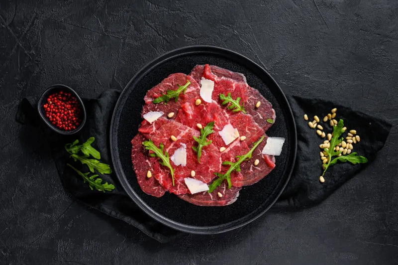 marbled beef carpaccio with arugula and parmesan cheese black background top view space for text
