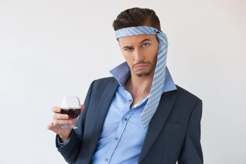 closeup of drunk business man looking at camera, wearing tie on his head and holding glass of wine isolated view on white background