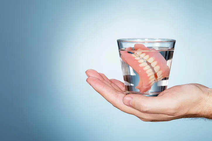 man holding a glass containing old dentures