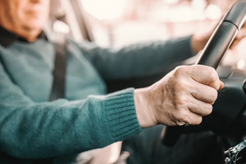 close up of senior man holding hands on steering while and driving his car