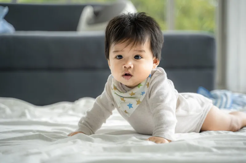 an asian baby is crawling along the floor on a room covered by a quilt