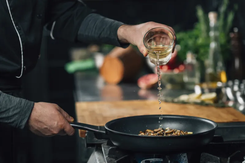 chef pouring white wine into a frying pan with sliced shiitake mushrooms