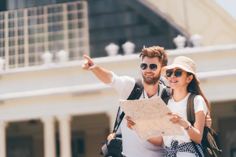 multiethnic traveler couple using generic local map together on sunny day, man pointing toward copy space honeymoon trip, backpacker tourist, asia tourism, or holiday vacation travel concept