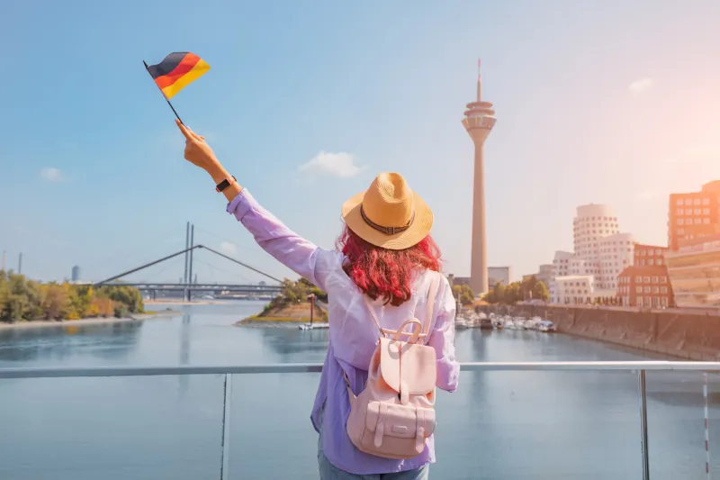 a young happy asian girl with a german flag poses at the media harbor and tv-tower in dusseldorf studying language abroad and traveling concept