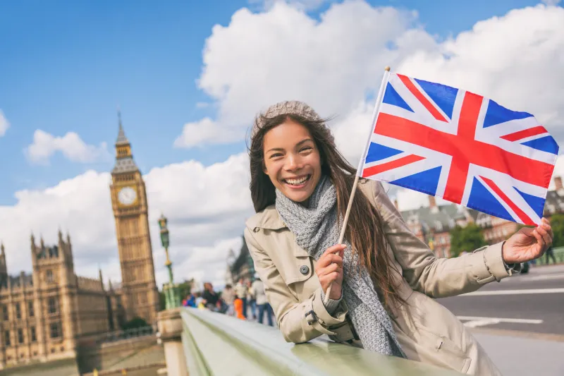 london travel tourist woman showing union flag great britain british uk flag asian girl at big ben on westminster bridge on europe holidays holding icon at iconic landmark