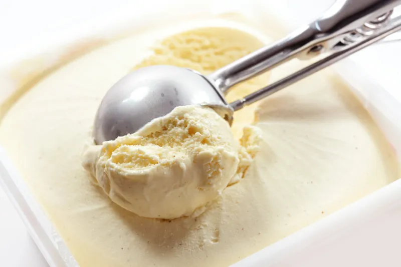metal scoop scrapes vanilla ice cream from the box, copy space, selected focus, narrow depth of field