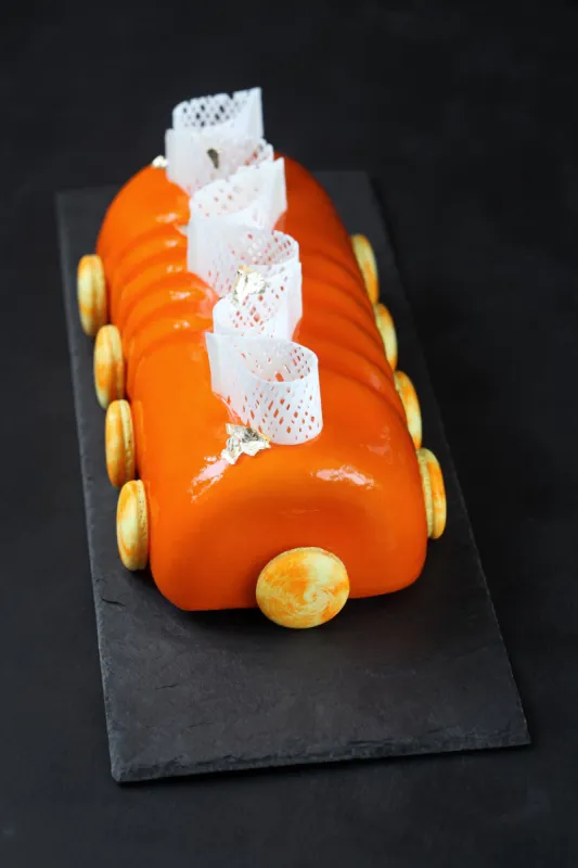 contemporary orange yule log decorated with french macarons and white chocolate elements, on black background