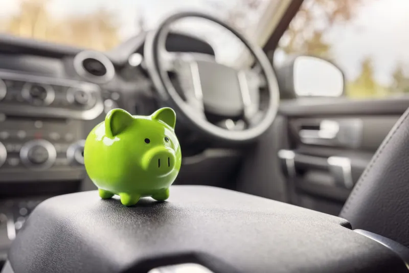 green piggy bank money box in car interior, vehicle purchase, insurance or driving and motoring cost