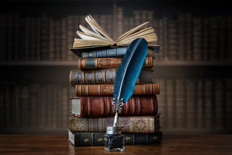 old books ,quill pen and vintage inkwell on wooden desk in old library ancient books historical background retro style conceptual background on history, education, literature topics