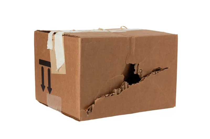 damaged crumpled postal cardboard box with a punched side and a black big hole poor delivery of goods