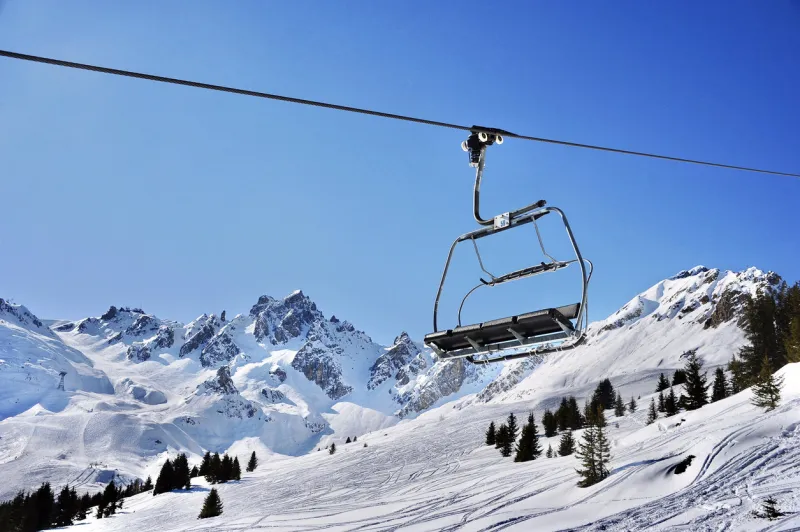 empty chair lift with blue sky over the snowy mountains