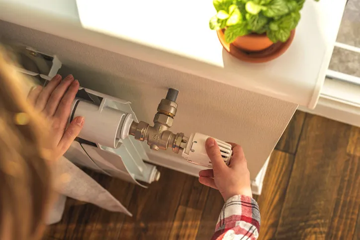 woman adjusting the temperature on valve of a radiator at home, modern interior background photo