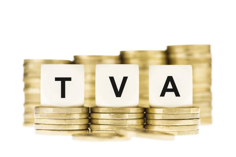 taxation concept the letters tva (french value added tax) on dice on piles of gold coins on a white background