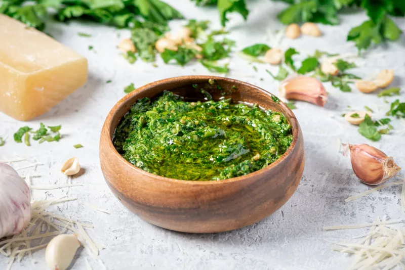 homemade pesto sauce in a wooden bowl and ingredients for cooking on a gray background close-up italian food