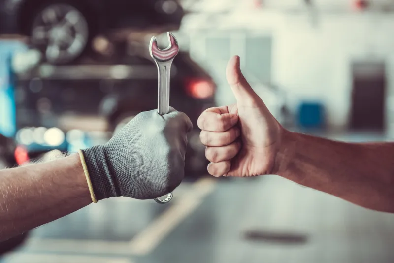cropped image of mechanics working in auto service one is holding a spanner while the other is showing ok sign