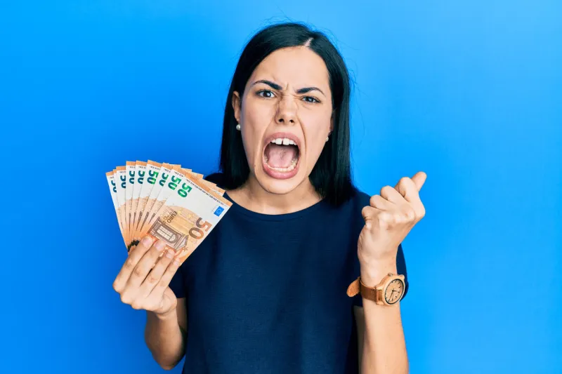 beautiful young woman holding bunch of 50 euro banknotes angry and mad raising fist frustrated and furious while shouting with anger rage and aggressive concept