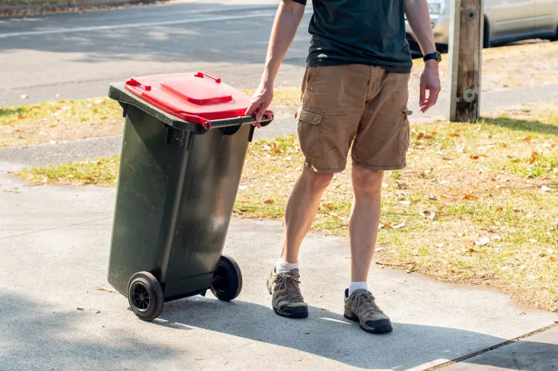a man dragging the household wheelie red bin with general waste on the street for council gargbage collection waste management concept