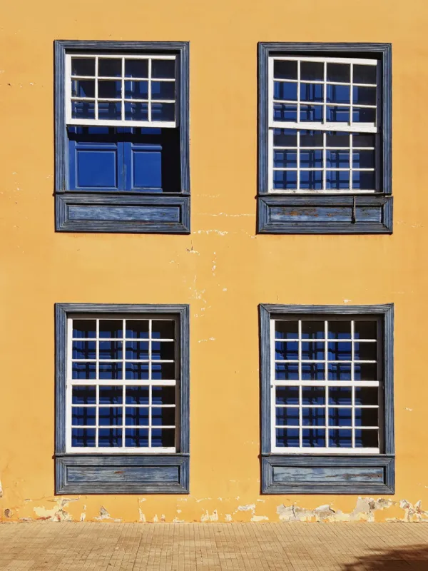 fragment of the old facade with closed vintage windows traditional guillotine windows front view four old style blue wooden windows on a bright orange wall construction, architecture pattern