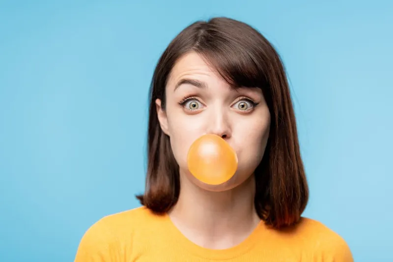 young amazed brunette staring at you while blowing chewing-gum bubble in front of camera