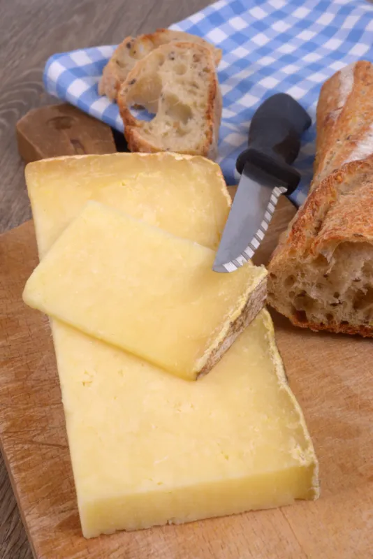 pieces of laguiole cheese with a knife on a cutting board next to a piece of bread in close-up