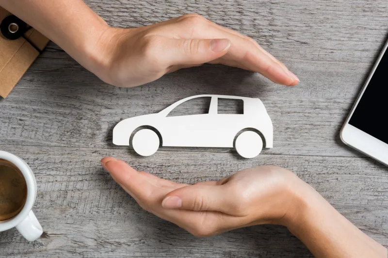 hands protecting icon of car over wooden table top view of hands showing gesture of protecting car car insurance and automotive business concept