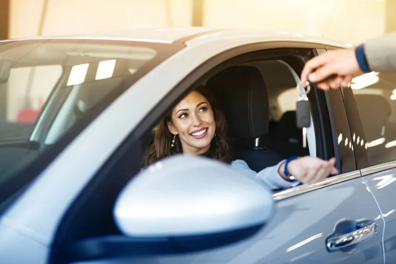 an attractive brunette woman sitting in her brand new car and taking keys from vehicle dealer